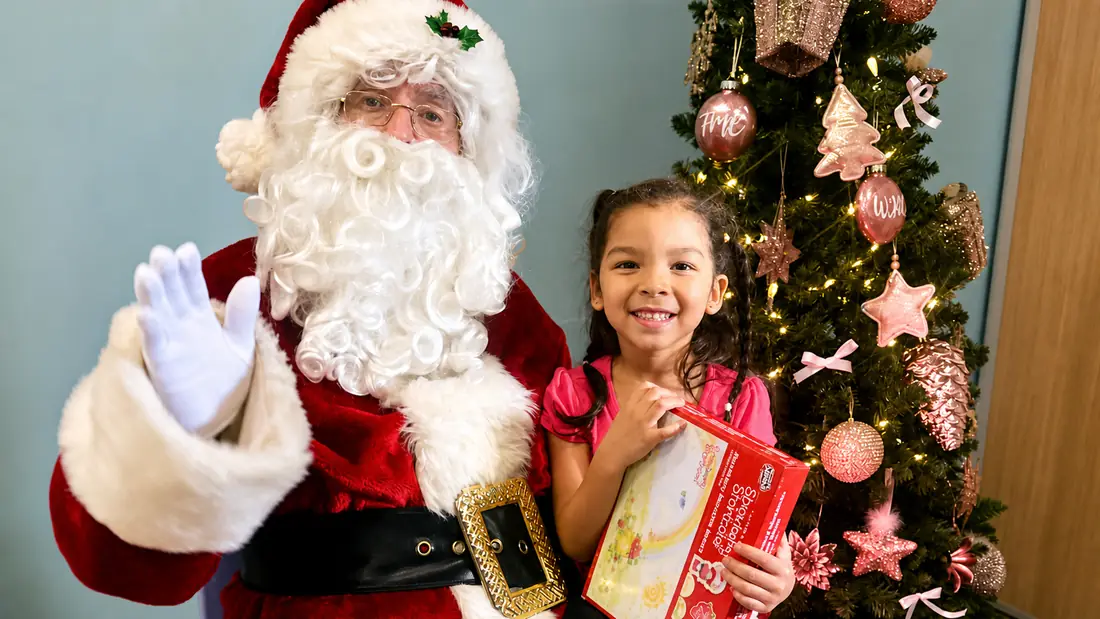 Child holding a gift near Santa during an APAG Cares holiday event