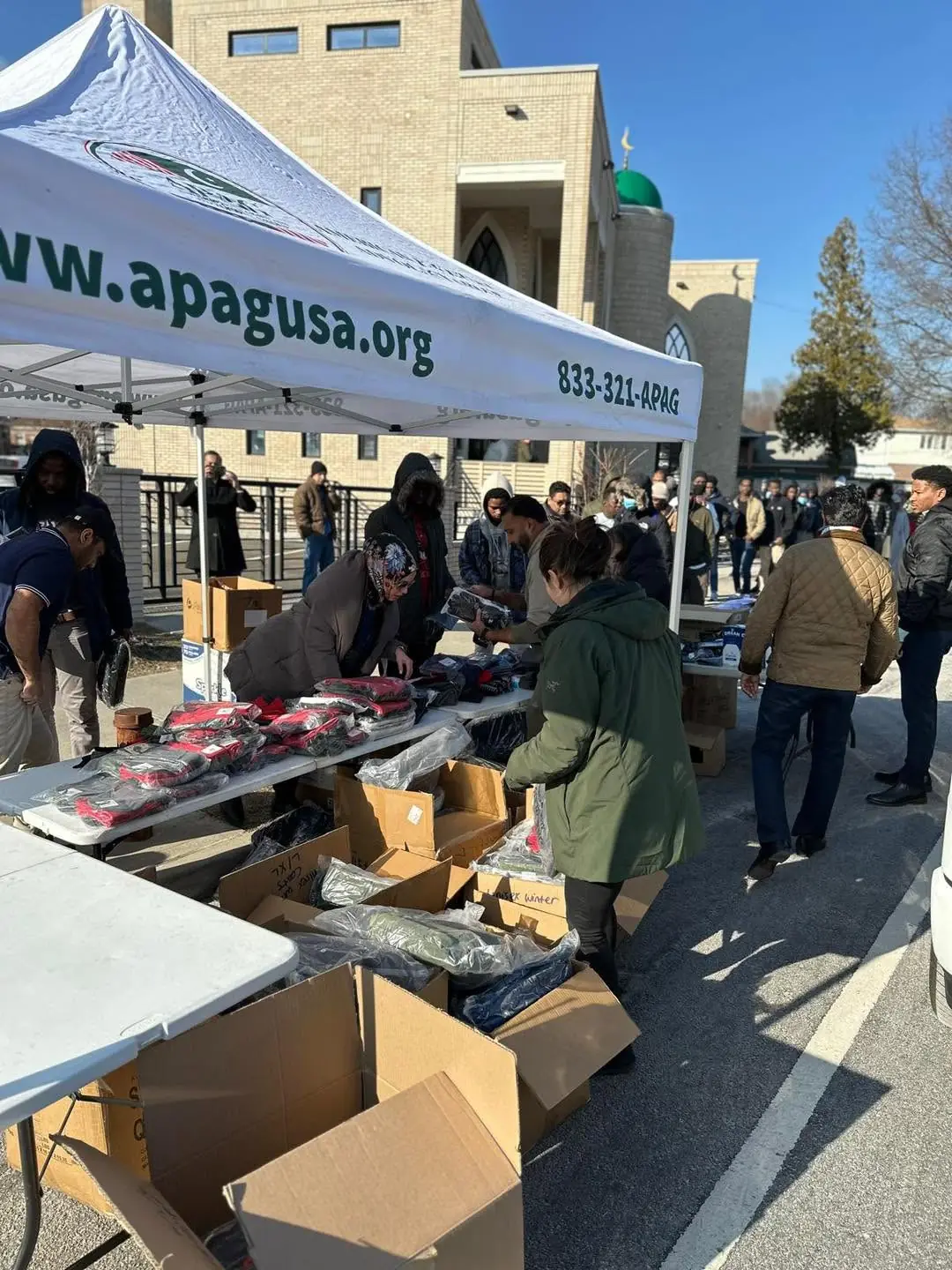 Community members receiving winter clothing under an APAG Cares canopy